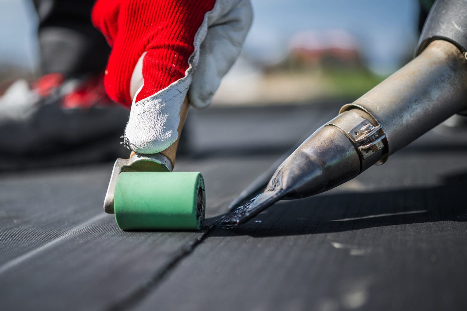 Roof Worker Attaching Pieces of EPDM Membrane Roofing Material Using Hot Air Blower and Industrial Roller.